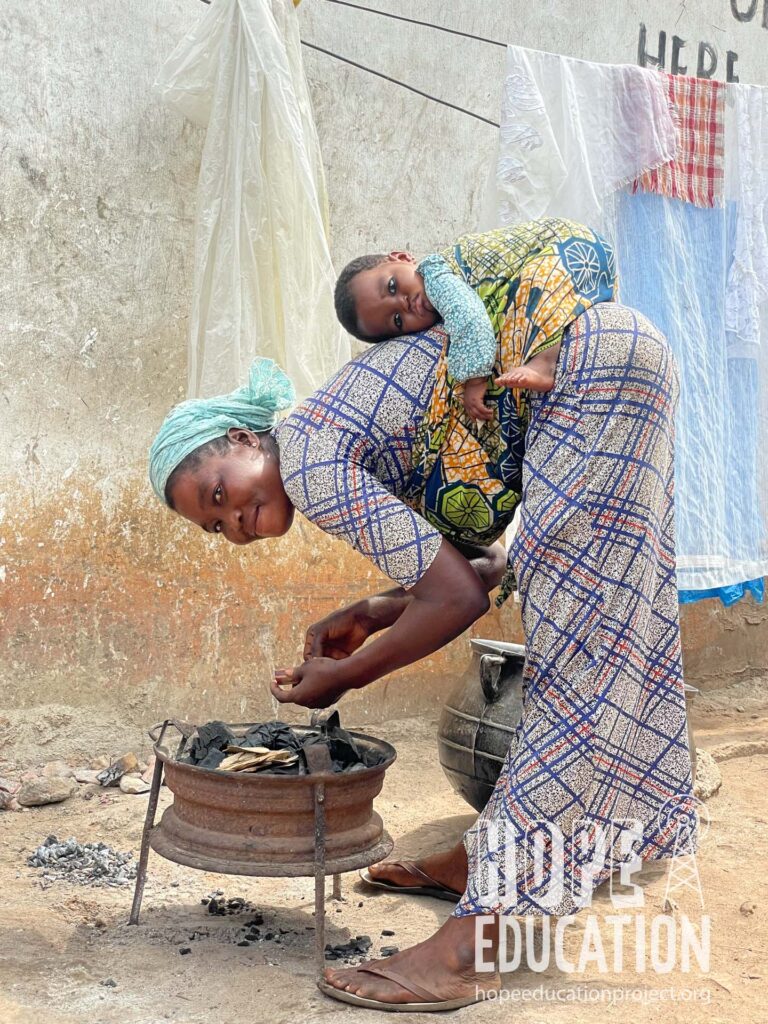 A Mamprusi kayaye with baby on her back lighting a fire to start making banku