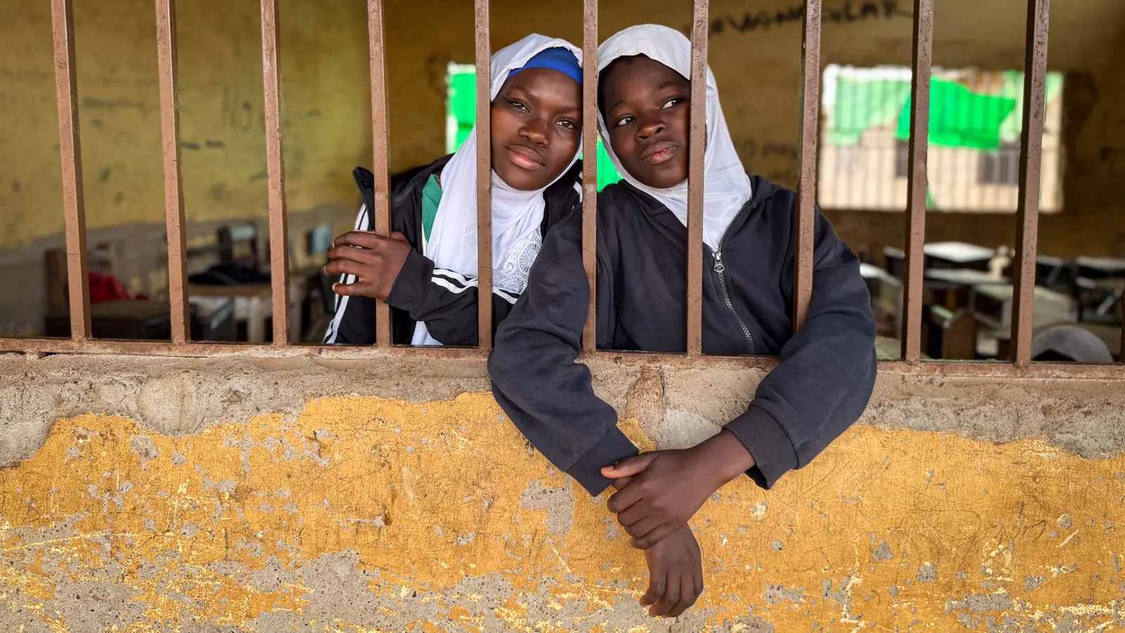 Two schoolgirls look out through a classroom window in Tamale