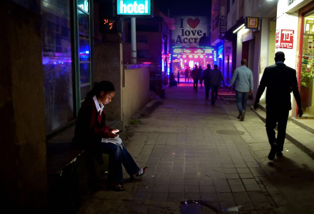 Porta Potty party in Ghana, a young sex worker checks her phone looking at an escort website in Accra, looking for clients interested in Porta Potty.