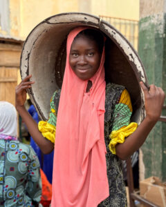 A young girl working as a kayaye in Tamale's Central Market with a head pan on her head - kayaye are at high risk of human trafficking in Ghana 